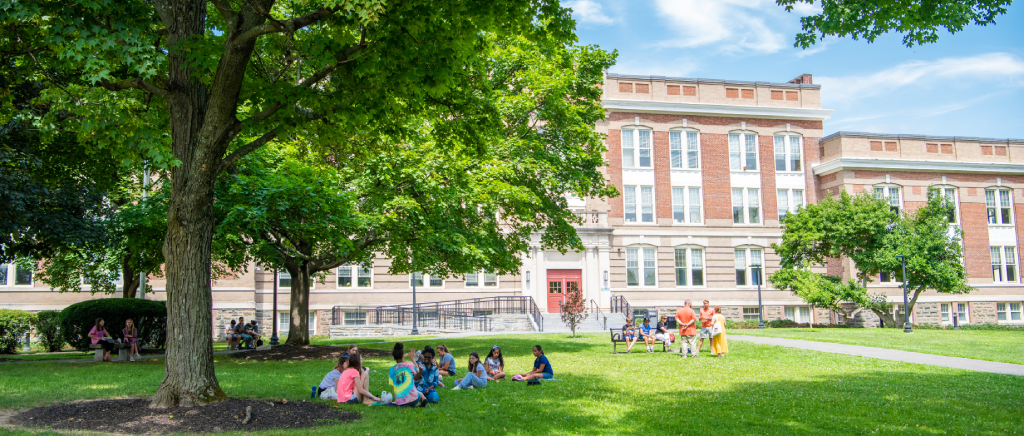 Several students sitting on the quad lawn outside the Old Main building at SUNY New Paltz.